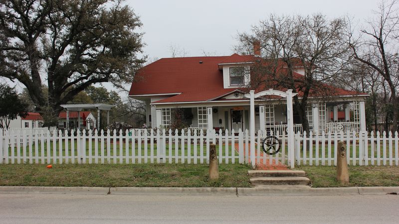 A historic house with a red roof behind a white picket fence in Belton