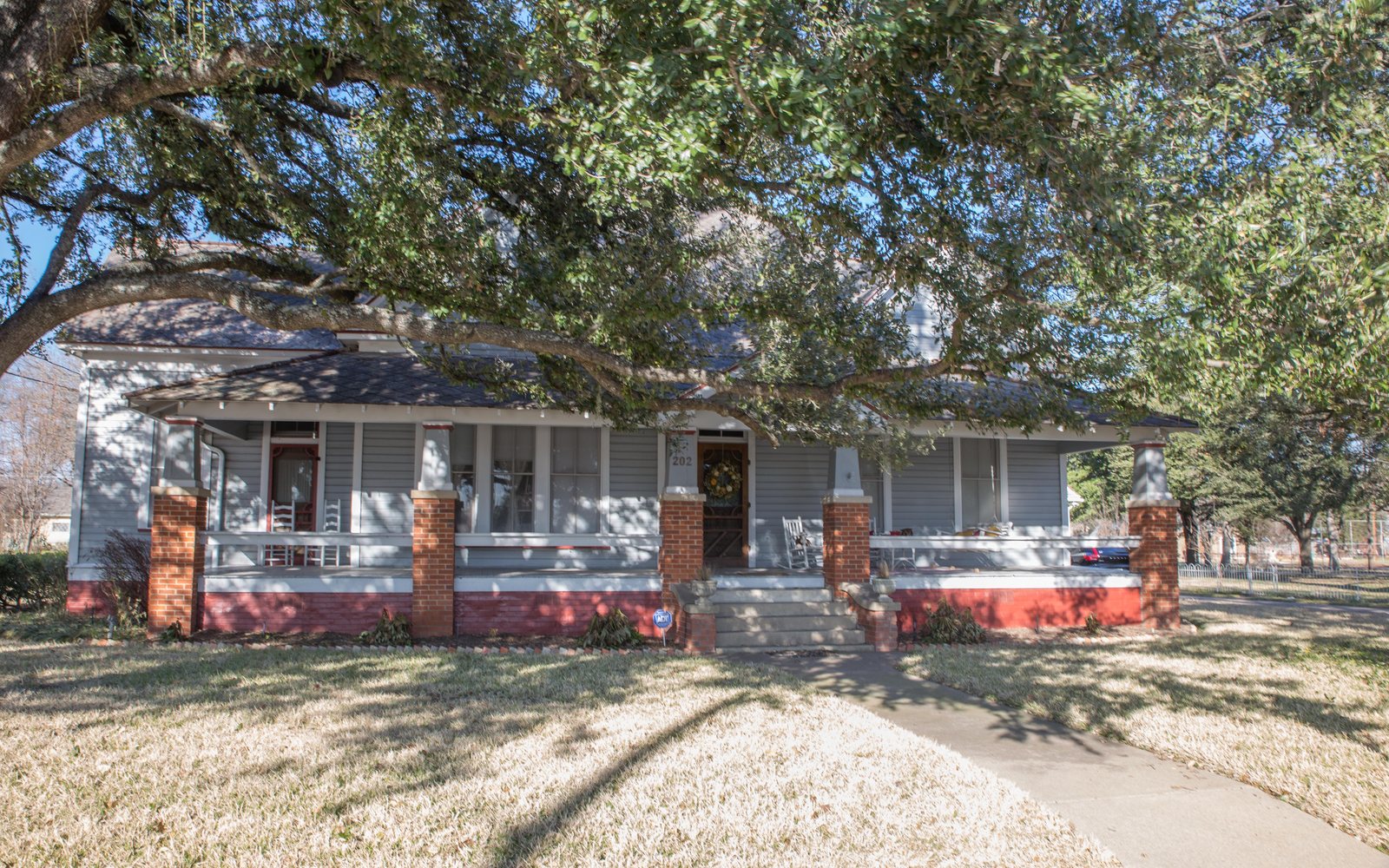 A one-story house with a long porch under a large oak in Cameron